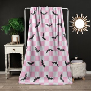 May include: Pink and white checkered throw blanket with a black bat pattern.