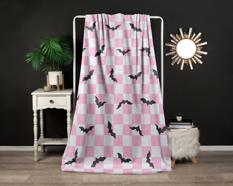 May include: Pink and white checkered throw blanket with a black bat pattern.