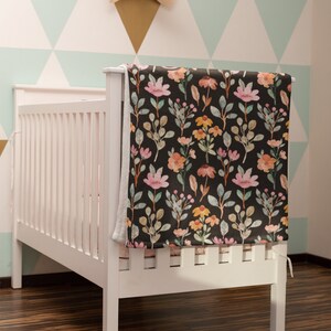 May include: A white crib with a floral patterned blanket draped over the side. The blanket features a dark background with pink, orange, and yellow flowers and green leaves. A plush elephant head decorates the wall.