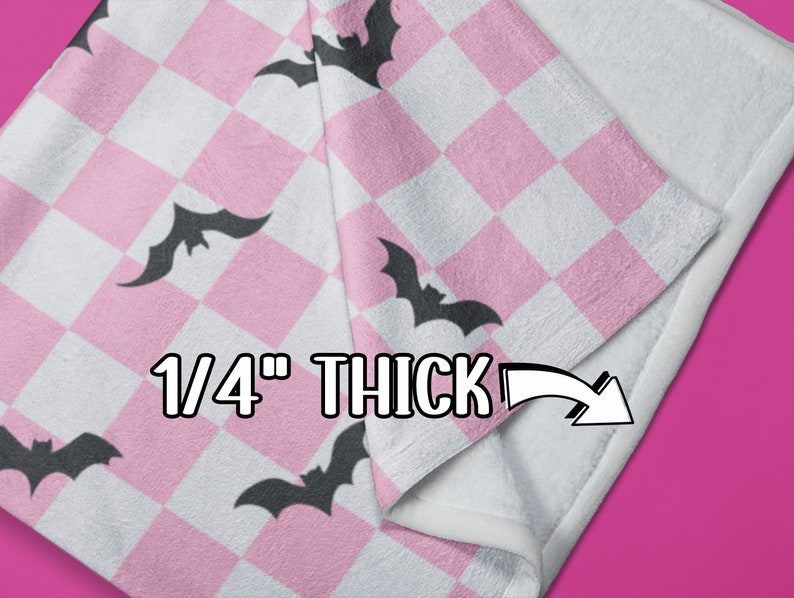 May include: Pink and white checkered fleece blanket with black bat silhouettes. The blanket is folded to show the 1/4 inch thickness.
