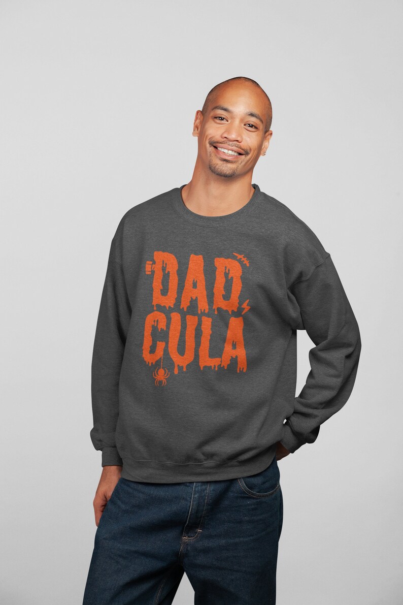 May include: A dark gray sweatshirt with a graphic print of the text "DAD-CULA" in orange. The text is dripping and has a spider and lightning bolt graphic.