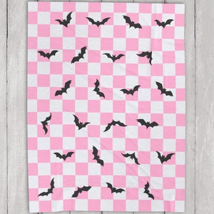 May include: Pink and white checkered throw blanket with a black bat pattern.
