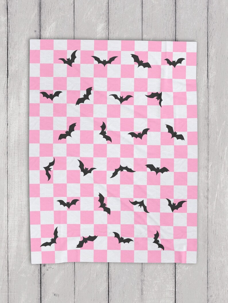 May include: Pink and white checkered throw blanket with a black bat pattern.