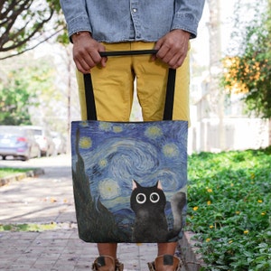 May include: A black tote bag with a black cat silhouette on a blue and yellow starry night background. The bag has black straps.