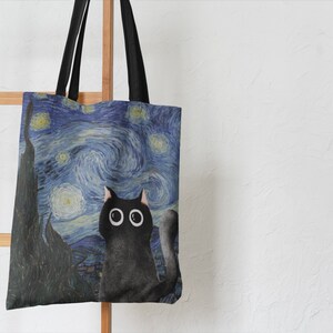 May include: A black canvas tote bag with a print of a black cat looking up at a starry night sky. The sky is blue and yellow with swirling clouds and white stars.