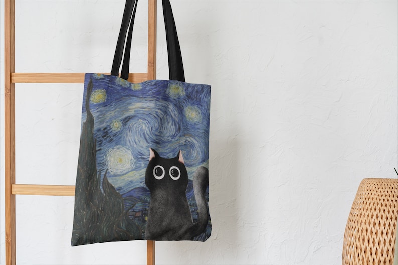 May include: A black canvas tote bag with a print of a black cat looking up at a starry night sky. The sky is blue and yellow with swirling clouds and white stars.