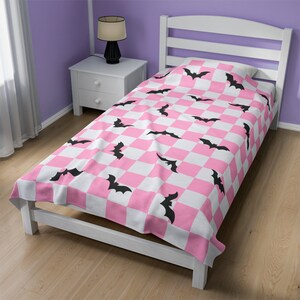 May include: Pink and white checkered twin-sized bedspread with a black bat pattern.