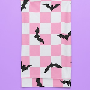 May include: Pink and white checkered fabric with black bat silhouettes. The fabric is folded in half and appears to be a throw blanket.