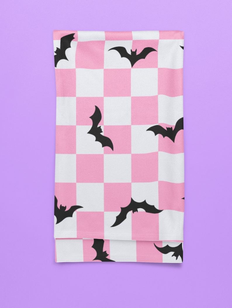 May include: Pink and white checkered fabric with black bat silhouettes. The fabric is folded in half and appears to be a throw blanket.