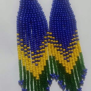 Puede incluir: Un par de pendientes largos colgantes hechos de pequeñas cuentas de semillas. El diseño presenta un patrón degradado que comienza con azul profundo en la parte superior, pasa a amarillo brillante y termina con flecos verde oscuro con cuentas azules.