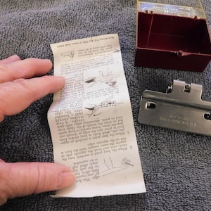 May include: A Buck Hone Master knife sharpener with a red and clear plastic case, a metal sharpening guide, and a folded instruction sheet. The instruction sheet has diagrams and text.