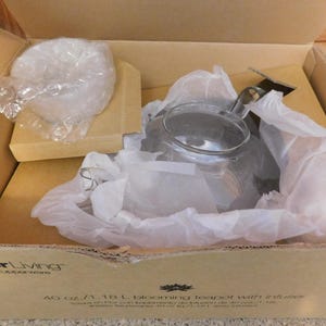 May include: A white ceramic mug with a black handle and the text "But First, Coffee" in a black, handwritten-style font. The mug is on a white surface.