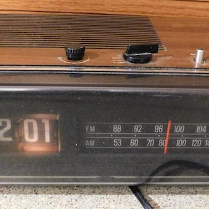 May include: Vintage Panasonic digital clock radio with a wood grain top and black front panel. The clock displays 12:01 in orange digits. Features AM/FM radio dial and control knobs. The brand name "Panasonic" is printed on the front.
