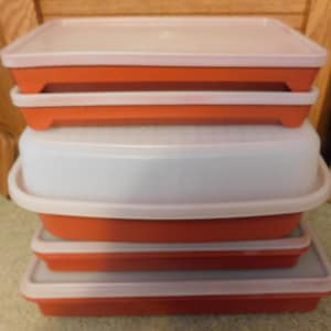 May include: A stack of orange and white plastic food storage containers with lids. The containers are rectangular and appear to be empty. The lids are white and fit snugly on top of the orange bases.