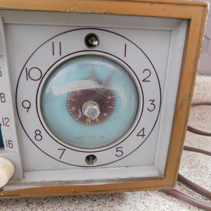 Puede incluir: Radio reloj vintage con esfera azul claro y marco de madera marr&oacute;n. La esfera del reloj tiene n&uacute;meros y manecillas negras. El dial de la radio est&aacute; en el lado izquierdo con perillas blancas.