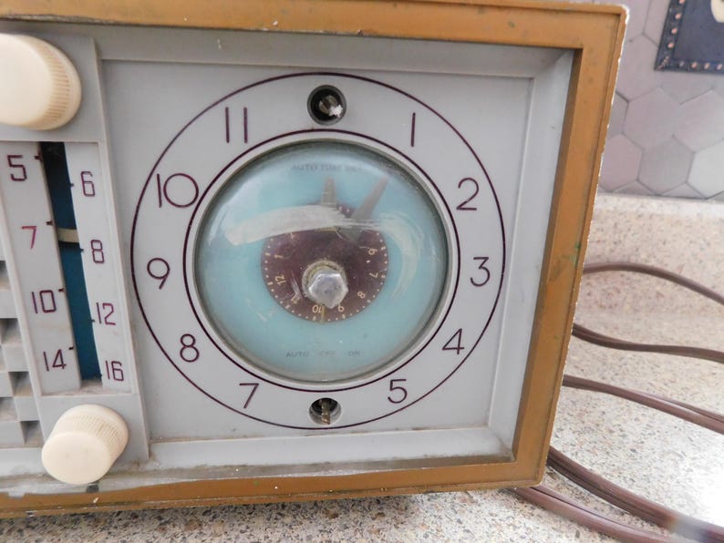 Puede incluir: Radio reloj vintage con esfera azul claro y marco de madera marr&oacute;n. La esfera del reloj tiene n&uacute;meros y manecillas negras. El dial de la radio est&aacute; en el lado izquierdo con perillas blancas.