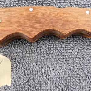 K&ouml;nnte beinhalten: Ein Klappmesser mit einem Holzgriff mit wellenf&ouml;rmigem Design. Der Griff ist mit kleinen silbernen Nieten befestigt. Die Klinge ist teilweise sichtbar, und ein kleines Etikett mit der Nummer "4" befindet sich im Vordergrund.