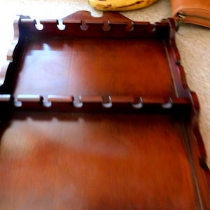 May include: A two-tiered, wooden spoon rack with a rich, dark brown finish. The rack features scalloped edges and small, circular cutouts for holding spoons. The top tier has a decorative cutout at the top. The rack is designed to be mounted on a wall.