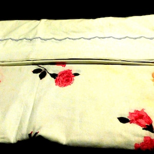 May include: Cream-colored pillowcase with a floral pattern featuring red roses and black leaves. The pillowcase has a scalloped edge with a gray trim. Decorative scrollwork in orange is also visible.