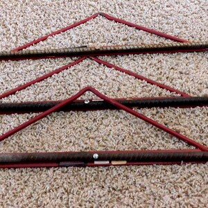 May include: Three metal clothes hangers with red support structures and silver hooks. The hangers are made of rough, dark metal and are arranged in a row. The red supports form triangular shapes, adding a decorative element to the functional design.
