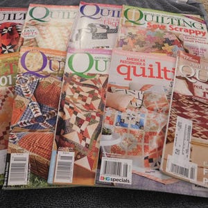 May include: A collection of quilting magazines with colorful quilt patterns on the covers. Titles include "Quilting," "American Patchwork & Quilting," and "Quilt 101." The magazines feature various quilt designs and techniques.