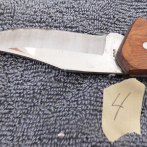 K&ouml;nnte beinhalten: Ein Edelstahlmesser mit Holzgriff. Die Klinge ist gebogen und hat eine scharfe Schneide. Der Griff ist braun und hat einen wei&szlig;en Punkt. Ein St&uuml;ck Klebeband mit der Nummer 4 befindet sich im Bild.