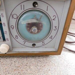 Puede incluir: Primer plano de una radio vintage con reloj. La radio tiene una cara gris claro con un reloj con fondo azul claro y manecillas marrones. El marco de la radio es de color marr&oacute;n c&aacute;lido y tiene perillas blancas y un dial.