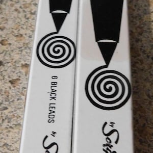 May include: Two white Scripto boxes. One reads "LONG LEAD 20¢" and the other "MECHANICAL TYPEWRITER ERASERS 20¢". Both have a black spiral design and the Scripto logo. One box says "6 BLACK LEADS".