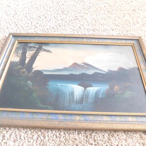May include: A framed landscape painting depicting a waterfall cascading into a lake, with mountains in the background. The artwork features a blue and gold frame. The painting's colors include blues, greens, and earth tones.