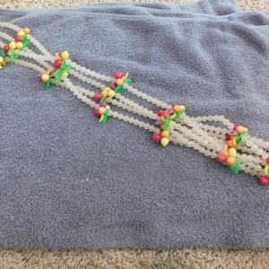 May include: A multi-strand necklace featuring translucent clear beads arranged in a lattice pattern. The design is accented with small clusters of colorful red, yellow, and green fruit-shaped beads spaced evenly along the length of the strands.