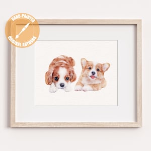 May include: Watercolor painting of two adorable puppies, one a Cavalier King Charles Spaniel and the other a Corgi, lying down. The artwork is framed in a light wood frame and includes a circular emblem that reads "HAND-PAINTED ORIGINAL ARTWORK."