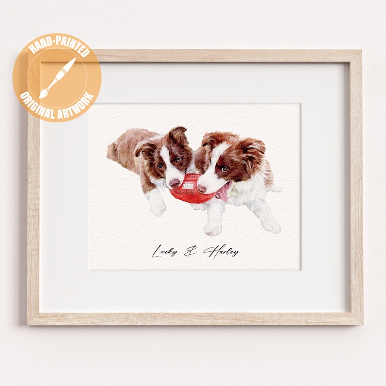 May include: A framed watercolor painting featuring two brown and white puppies playing with a red ball. The artwork is hand-painted and labeled "Original Artwork." The names "Lucky & Harley" are written below the dogs.