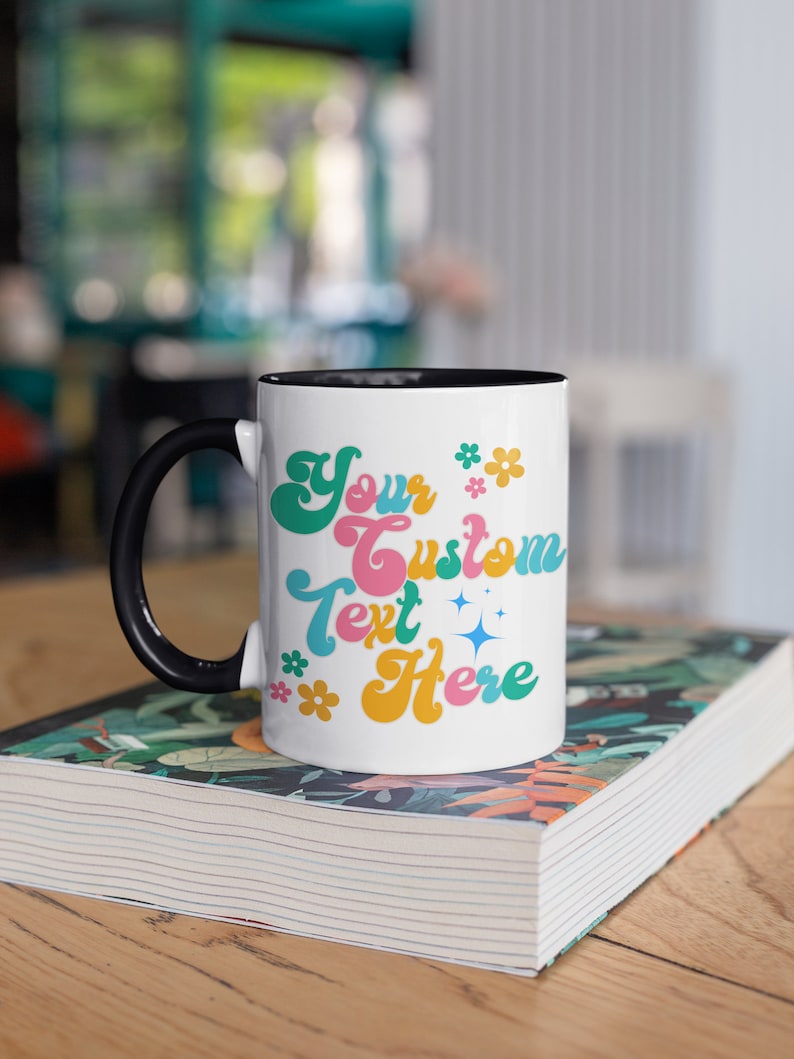 May include: White ceramic mug with a black handle and black rim. The mug has a colorful retro design with the text "Your Custom Text Here" and small flower and star accents.