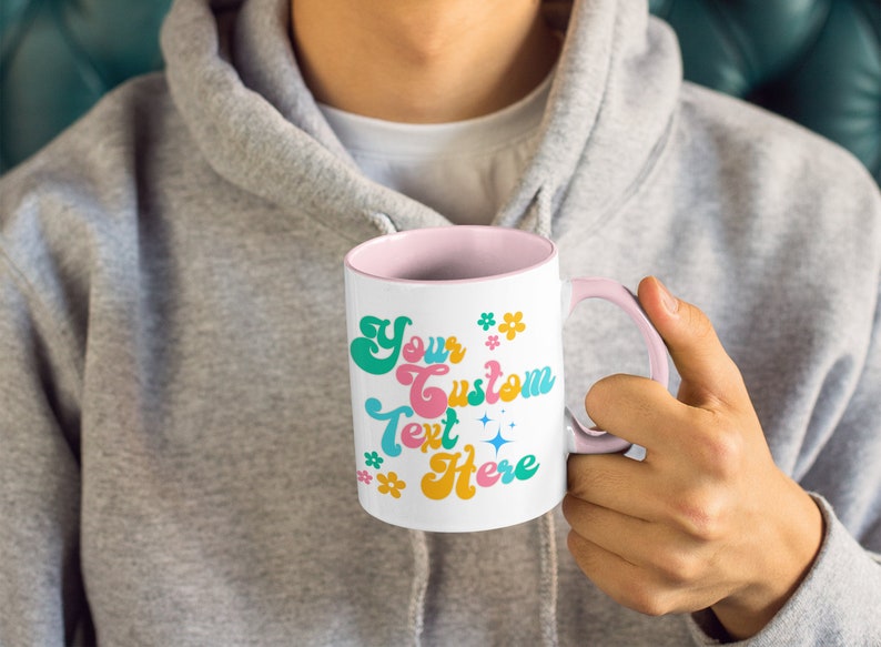 May include: White ceramic mug with a pink rim and handle. The mug has a retro-style design with the text "Your Custom Text Here" in colorful letters and flowers.