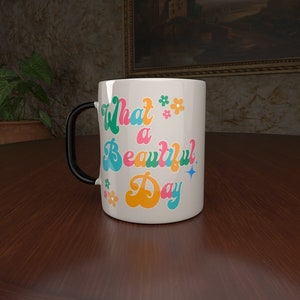 May include: White ceramic mug with a black handle. The mug has a colorful retro design with the text "What a Beautiful Day" and small flower accents.
