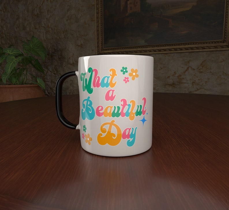 May include: White ceramic mug with a black handle. The mug has a colorful retro design with the text "What a Beautiful Day" and small flower accents.