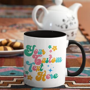 May include: White ceramic coffee mug with a black rim and handle. The mug has a colorful retro design with the text "Your Custom Text Here" and flowers.