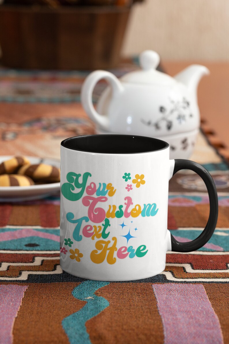 May include: White ceramic coffee mug with a black rim and handle. The mug has a colorful retro design with the text "Your Custom Text Here" and flowers.