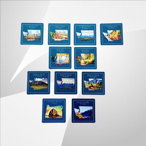 May include: Set of ten blue square coasters with a white outline and a colorful image of the state of Washington. Each coaster features a different city name and a unique image of a landmark or scenic view. The cities featured are Carnation, Duvall, North Bend, Cannon Beach, and Snoqualmie.