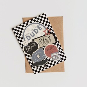 Pode incluir: Um cartão de aniversário com fundo xadrez e adesivos. O cartão diz "New Dudes Arrive" e "Scout's Turning Five". Os adesivos dizem "Dude", "July First", "Scout's House", "Rock On", e "Party in the Classic".