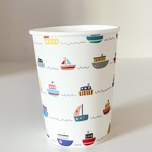May include: A white paper cup decorated with colorful cartoon boats and wavy lines. The boats are in various colors, including yellow, blue, red, and orange. The cup is designed for beverages.