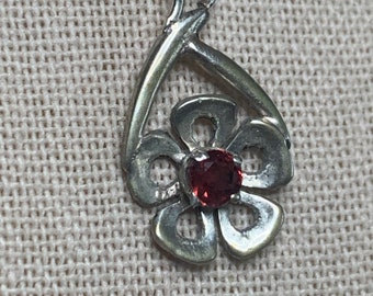 Srebrny wisiorek z granatem w oprawie kwiatowej. Granat jest okrągły o średnicy 4 mm.