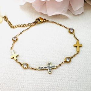 May include: Gold tone stainless steel bracelet with a delicate chain and four small cross charms. Each cross charm is embellished with clear cubic zirconia stones. The bracelet has a lobster claw clasp.