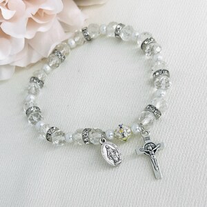 May include: A white crystal and pearl bracelet with a silver charm of the Virgin Mary and a silver crucifix.