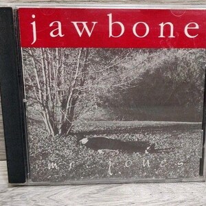 May include: A compact disc case featuring a black and white photograph of a tree and a field. The top section has a red horizontal bar with the white text jawbone. The bottom section contains the white text mr. jones centered on the image.