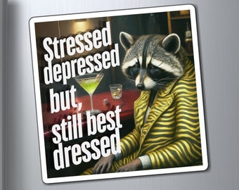 May include: A humorous magnet featuring a raccoon wearing a yellow and black striped suit and holding a martini glass. The text on the magnet reads "Stressed depressed but, still best dressed."