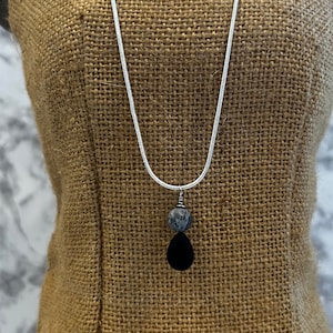 May include: A silver chain necklace with a black teardrop pendant and a grey and white bead.