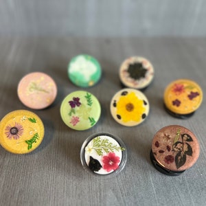 May include: Eight round resin trinket dishes with different pressed flower designs. The dishes are in various colors, including green, pink, yellow, and brown.