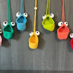 May include: Eight crocheted hanging baskets with googly eyes. The baskets are in various colors, including pink, green, blue, yellow, orange, and red.