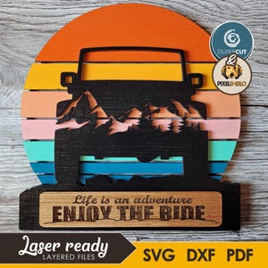 May include: A layered wooden sign featuring a black jeep silhouette set against a colorful sunset design. The sign includes the text "Life is an adventure, Enjoy the Ride." The bottom left corner reads "Laser ready, Layered files" with SVG, DXF, and PDF file formats.